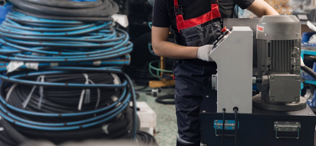 A technician is in a workshop using a hydraulic hose crimping machine to assemble a high-pressure